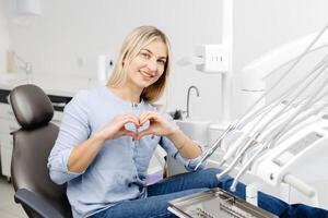 Patient showing heart shape with hands sitting in dentist chair photo
