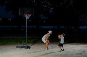 Father and son enjoy a night basketball game at a local park under bright lights focusing on teamwork and fun photo
