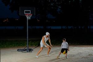 A father and son enjoy a night basketball game at a local park under bright lights focusing on teamwork photo