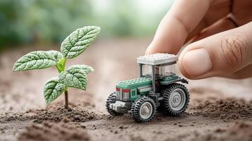 Toy tractor stands next to a young seedling on the ground. The concept of children's play, agriculture, ecology and the growth of a new plant photo