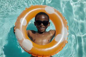 A joyful boy enjoys a summer day in a pool, wearing bright sunglasses and floating in a colorful ring, radiating happiness. The sun shines brightly, capturing the essence of summer joy photo