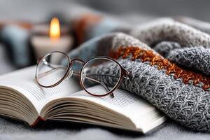 Cozy reading nook featuring a book, glasses, and a warm knitted blanket near a candle photo