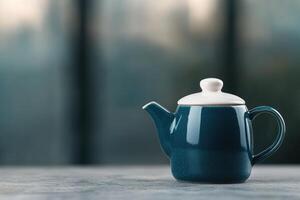 Elegant teal teapot placed on a rustic table with a blurred background showcasing a city view photo