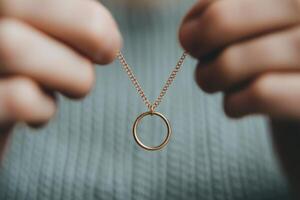 Hands holding a delicate gold necklace with a circular pendant in soft lighting photo