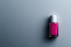 Bright pink nail polish bottle on a smooth grey surface showcasing vibrant color photo