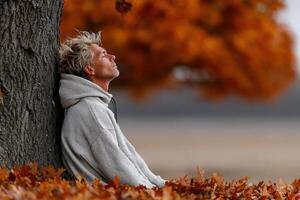 Man meditates under a tree surrounded by autumn leaves in a calm setting photo