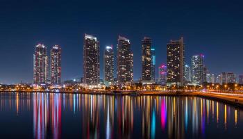 Nighttime cityscape with illuminated buildings reflecting on calm water and colorful vibrant lights photo