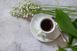 Beautiful lily-of-the-valley flowers, cup of coffee and greeting card on light background photo