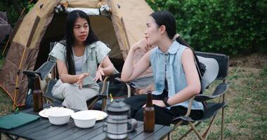 Handheld steady shot, Two Asian women sit together in a garden, happily chatting while enjoying snacks and drinks, surrounded by a cozy camping vibe. Holiday Activities video