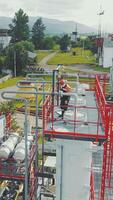Aerial view gas station operator climbs to the top of the station. Modern gas complex in the mountains. A gas worker climbs the ladder of the gas distribution unit against the backdrop of mountainous video