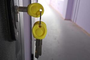 Yellow plastic-headed keys in lock on dark doorway in hallway setting photo