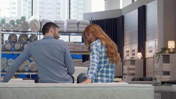 A joyful couple beams at the camera, seated on a plush orthopedic mattress in a modern furniture store. Surrounded by neatly arranged bedding and cozy furnishings, their excitement for creating a comfortable home is palpable video