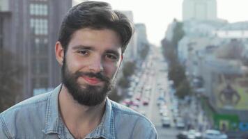 alegre jovem barbudo homem sorridente às a Câmera com uma vibrante cidade pano de fundo video