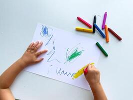 Child drawing with multicolored crayons on paper surface photo