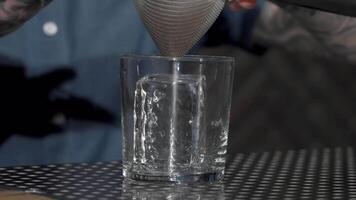 Cocktail being expertly poured into a glass over a gleaming cube of ice video