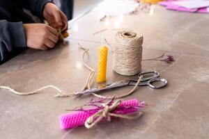 Young hands crafting beeswax candle with natural twine on marble surface photo