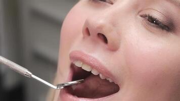 A close-up shot captures a dentist gently placing a dental mirror in a patient's mouth, showcasing a serene atmosphere. The cheerful blonde patient beams with a bright smile after her dental checkup, reflecting confidence and care in this clinical setting video
