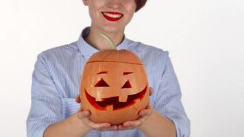 A joyful woman with striking red lips beams as she holds a delightfully carved Halloween pumpkin towards the camera. This vibrant scene captures the essence of autumn festivities, showcasing her playful spirit and the spooky charm of the jack-o'-lantern video