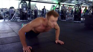 A focused young Caucasian athlete performs push-ups in a sleek gym, showcasing his muscular physique. With determination etched on his face, he embodies strength and discipline, pushing his limits on the black gym floor video