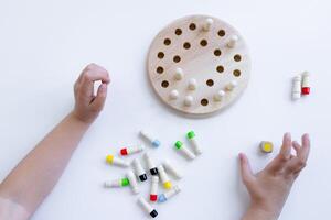 Child playing wooden memory game with colorful pegs and holes on white surface photo