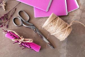 Crafting materials with pink wax sheets, scissors, jute twine, and dried flowers on stone surface photo