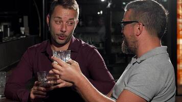 Two friends joyfully laughing and toasting with drinks at a lively bar video
