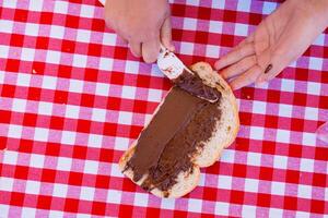 Spreading chocolate on bread at a picnic with red checkered tablecloth photo