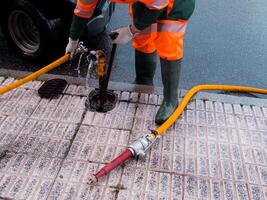 Worker in protective gear using hose for street drainage maintenance photo