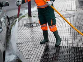 Municipal worker in high visibility gear cleaning pavement with hose on a rainy day photo