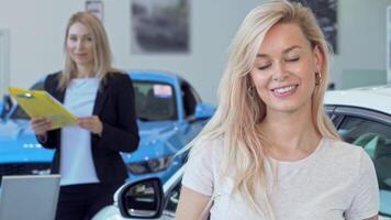 A joyful woman radiates happiness as she proudly holds her car keys, celebrating her new vehicle purchase. In the background, a professional saleswoman assists her, showcasing a vibrant dealership atmosphere filled with sleek automobiles video