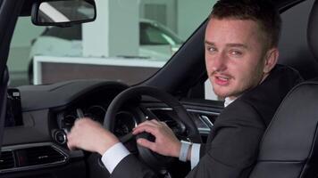Confident businessman proudly presenting car key while seated in sleek new automobile video