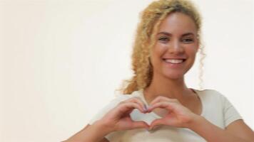 A cheerful red-haired girl beams with joy as she forms a heart shape with her hands against a soft white background. Her radiant smile and playful gesture create an atmosphere of love and positivity, perfect for celebrating connections and affection video