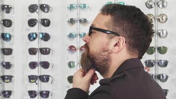 Thoughtful man selecting stylish sunglasses in an eyewear shop video