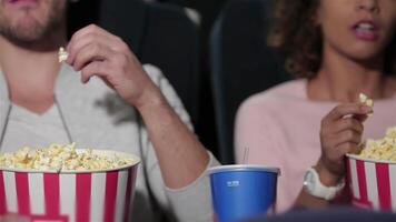 un alegre Pareja se sienta en un felpa cine teatro, compartiendo un grande Cubeta de palomitas de maiz mientras inmerso en el película magia. su la risa y emoción llenar el aire, creando un vibrante atmósfera de entretenimiento y conexión video