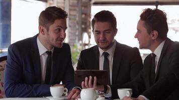 Engaged business team reviewing plans on a tablet during a lunch meeting video