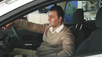 A satisfied man with dark hair sits comfortably at the steering wheel, admiring the sleek interior of a new car. His joyful expression radiates excitement, embodying the thrill of choosing the perfect vehicle video