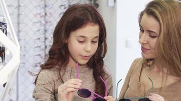 Joyful sisters trying on trendy sunglasses at a vibrant eyewear store video