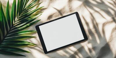 Modern tablet mockup on sandy background with tropical leaves for design and branding photo