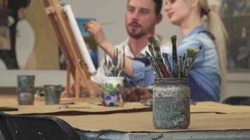 A joyful young couple, a man and a woman, are immersed in their artistic endeavor, surrounded by colorful paintbrushes and vibrant canvases. Their shared laughter and creativity fill the air, making this art studio a haven of love and inspiration video