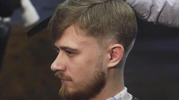 esta de cerca capturas un hermoso joven hombre sonriente con confianza como un experto Barbero expertamente adornos su pelo utilizando un eléctrico clíper. el atmósfera es vibrante y moderno, exhibiendo el arte de peluqueria en un elegante barbería ajuste video