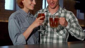 A cheerful couple enjoys a heartfelt embrace while sipping on refreshing beers at a charming pub. The warm ambiance, highlighted by rustic brick walls and soft lighting, enhances their connection, radiating love and joy in this delightful moment video