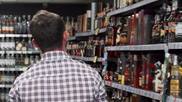 Man thoughtfully examining wine selections on supermarket shelves video