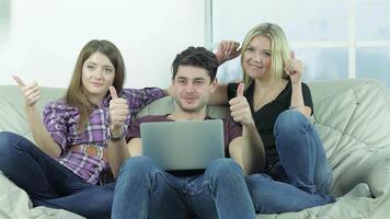 Three friends joyfully showing thumbs up while relaxing on a cozy couch video
