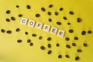 Word COFFEE Made of Wooden Tiles with Scattered Beans on Yellow Background Creative Caffeine Concept photo