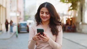 Indian woman use smartphone typing text messages browsing internet finishing work looking at camera video
