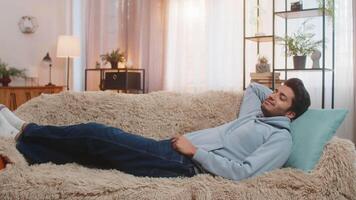 Tired Indian man lying on comfortable couch taking rest and daytime nap in living room at home video