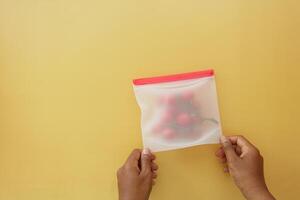 Hands holding a pouch with strawberries on a yellow background photo