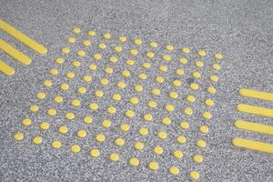 Textured ground surface with yellow tactile paving indicators photo