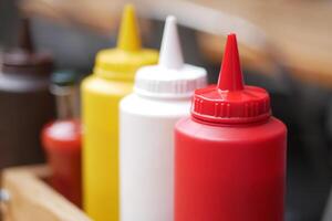 Colorful condiment bottles lined up on a rustic wooden table photo