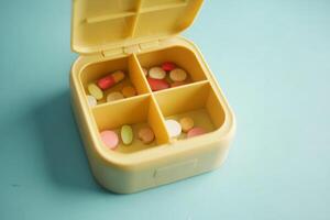 Pill organizer with various medications for daily use on blue surface photo